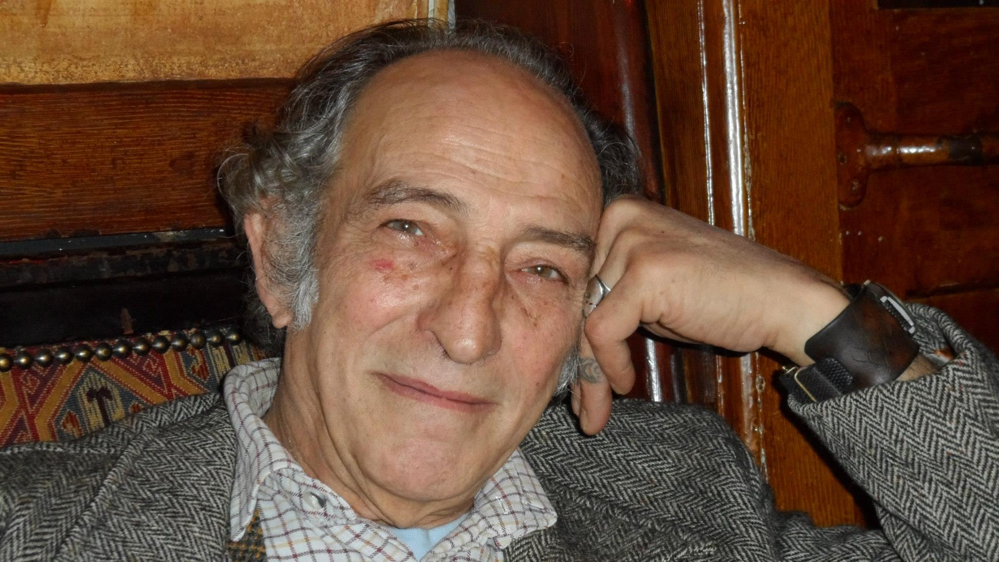 Gerry Temple, grey haired in a herringbone jacket, resting his head on his hand in a pub